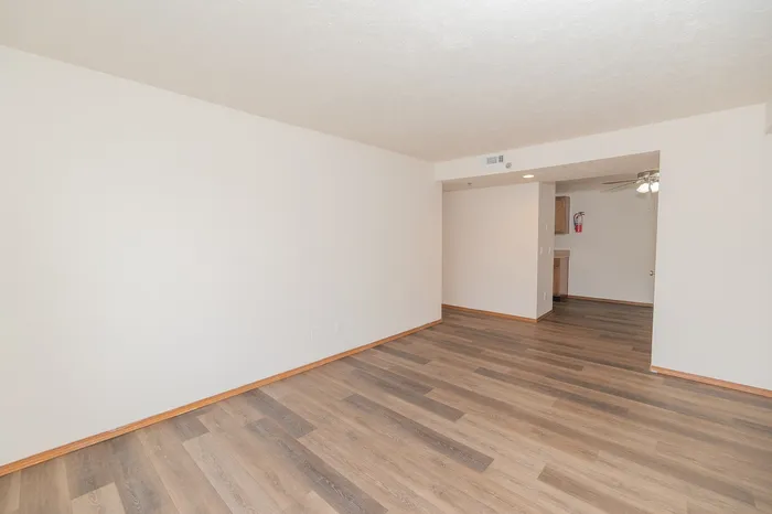 Bright and spacious living room with elegant wood flooring and neutral walls, leading into an inviting open kitchen area.