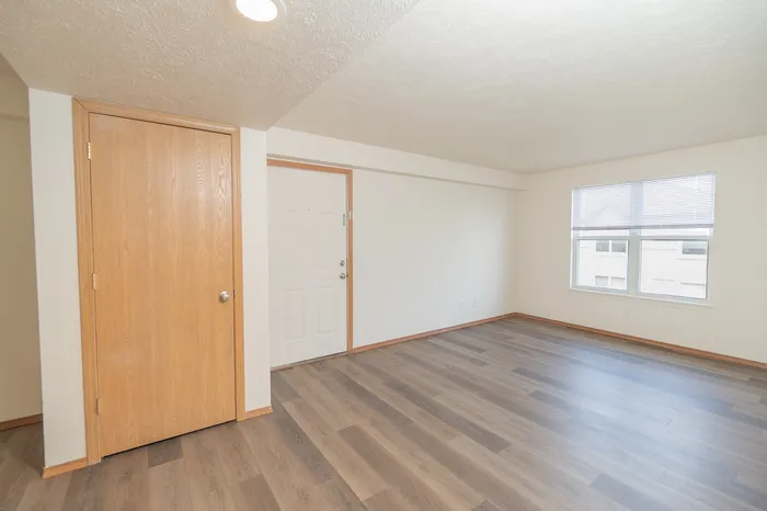 Bright and airy living space with elegant wooden flooring, a cozy corner, and a large window offering ample natural light.