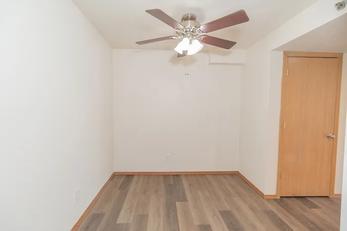Bright and versatile room with elegant wooden flooring and a stylish ceiling fan, perfect for cozy living.