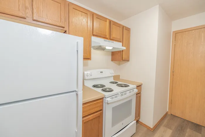 Charming kitchen boasting warm wooden cabinetry, modern electric stove, and sleek refrigerator enhancing a cozy cooking space.