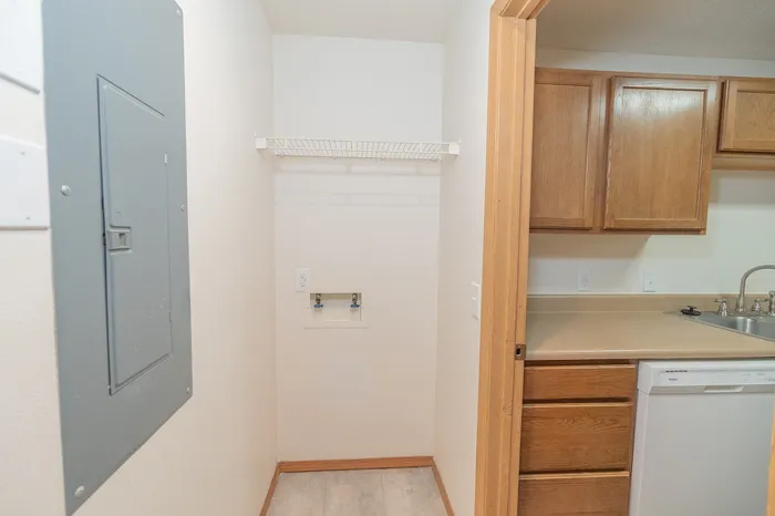 Cozy laundry nook adjacent to kitchen with wood cabinets, sleek countertop, and modern dishwasher.