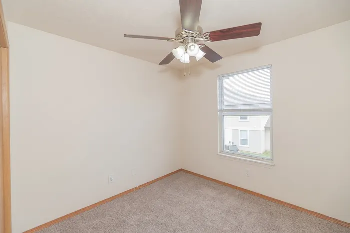 Bright and airy room with a ceiling fan, plush carpet, and a large window offering natural light.