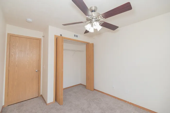 Inviting bedroom with cozy carpet, spacious closet, and elegant ceiling fan, ideal for comfort and relaxation.