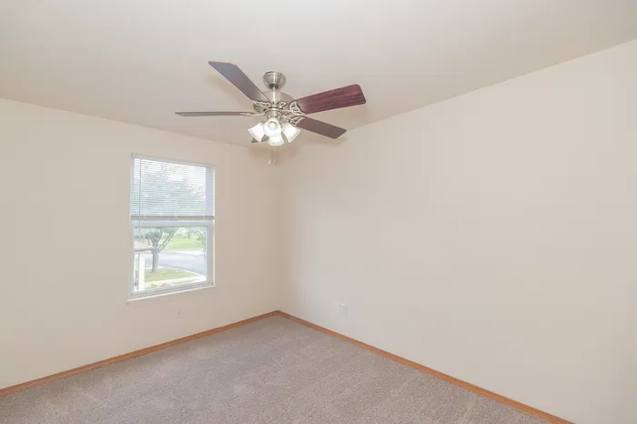 Bright and spacious bedroom with plush carpet, elegant ceiling fan, and a sunlit window offering serene views.