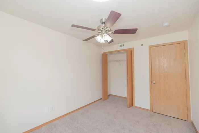 Bright and inviting bedroom with plush carpet, spacious closet, and modern ceiling fan, perfect for relaxing.