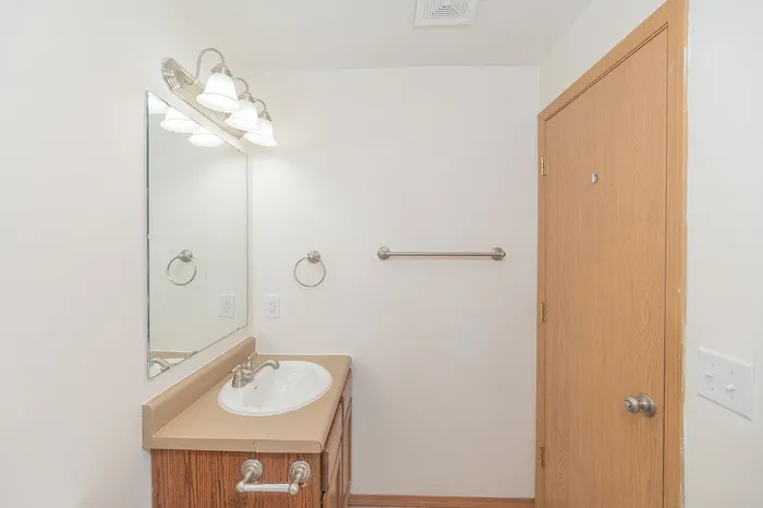 Bright and inviting bathroom with elegant fixtures, large mirror, and classic wood cabinetry for a touch of warmth.