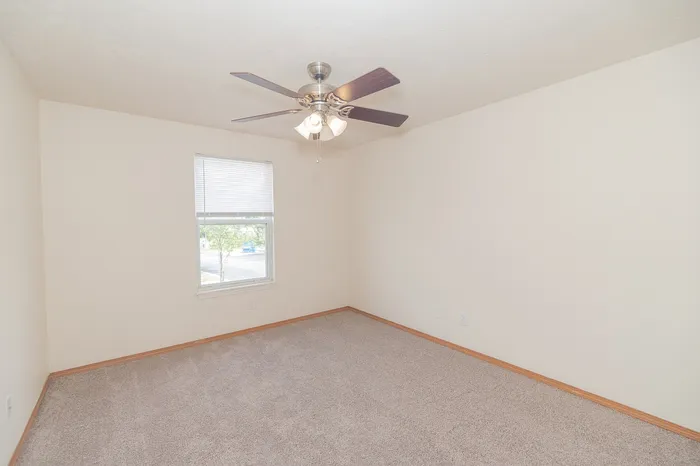 Bright and airy bedroom with plush carpet, ceiling fan, and large window for natural light.