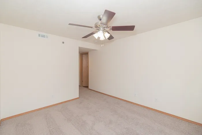 Bright and spacious room with plush carpeting and a stylish ceiling fan, perfect for a cozy living space.