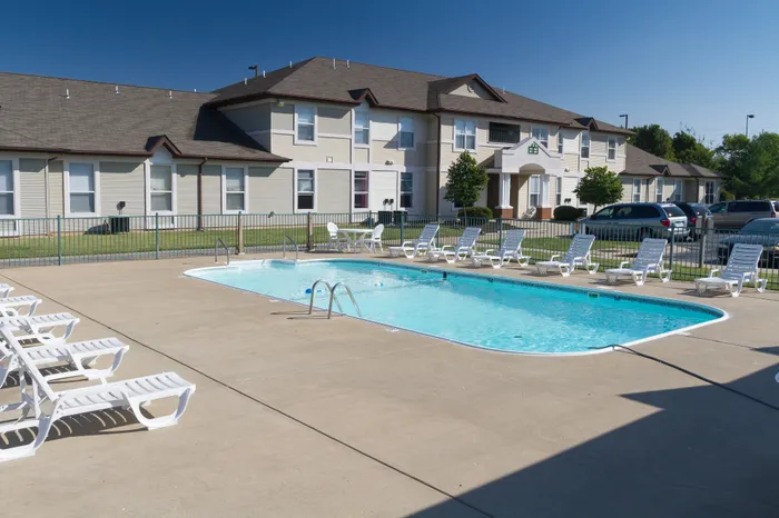 Charming apartment complex with a pristine outdoor pool, surrounded by comfortable sun loungers and manicured landscaping.