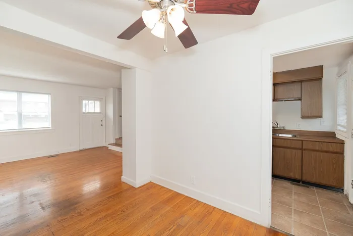 Bright open-plan living space with hardwood floors, modern ceiling fan, and cozy kitchen with wood cabinetry.