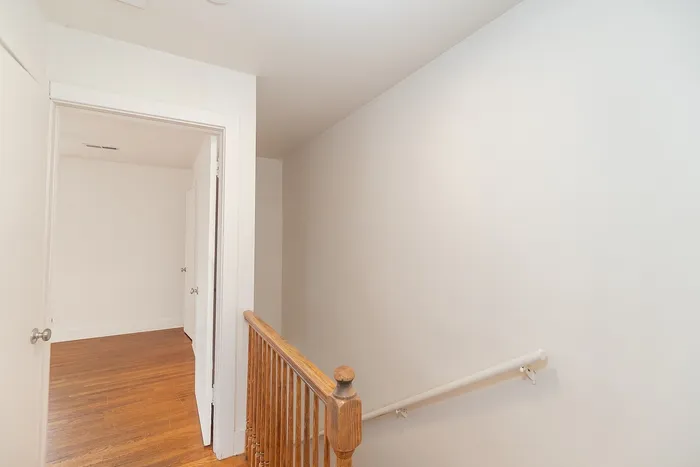 Bright and welcoming hallway with polished wooden floors and clean white walls, accented by an elegant wooden railing.
