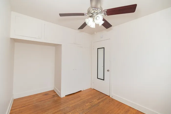 Bright and cozy room with elegant hardwood floors, a sleek ceiling fan, and built-in storage cabinets.