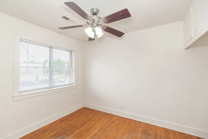 Bright and airy room with elegant hardwood floors and a sleek ceiling fan, offering a cozy ambiance and natural light from a large window.