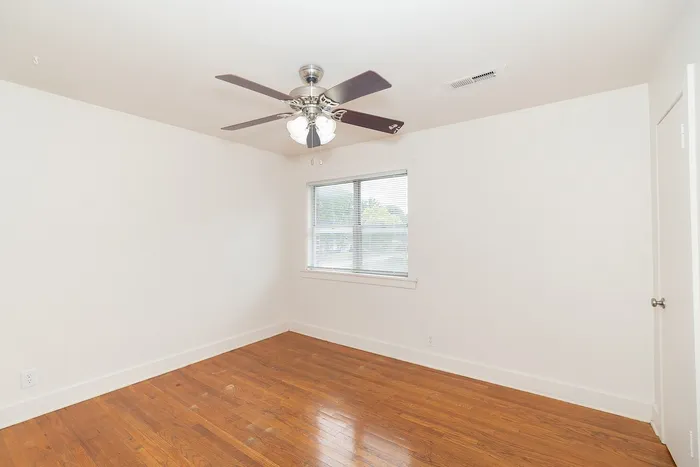 Bright and spacious room with elegant hardwood flooring and a sleek ceiling fan, perfect for a cozy living space.