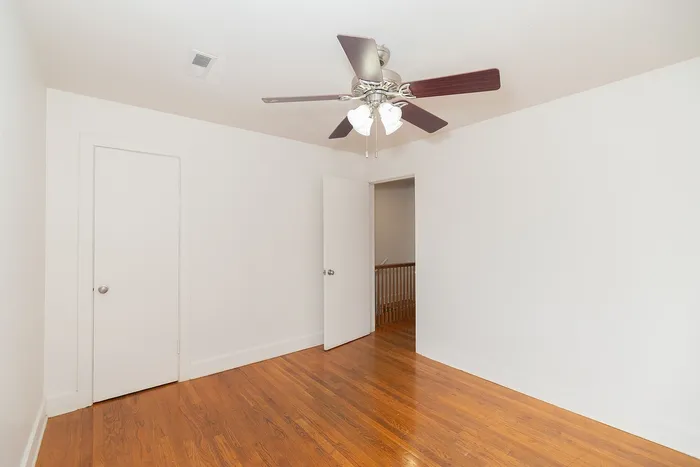 Bright, spacious room with polished hardwood floors, a modern ceiling fan, and a clean, freshly painted interior.