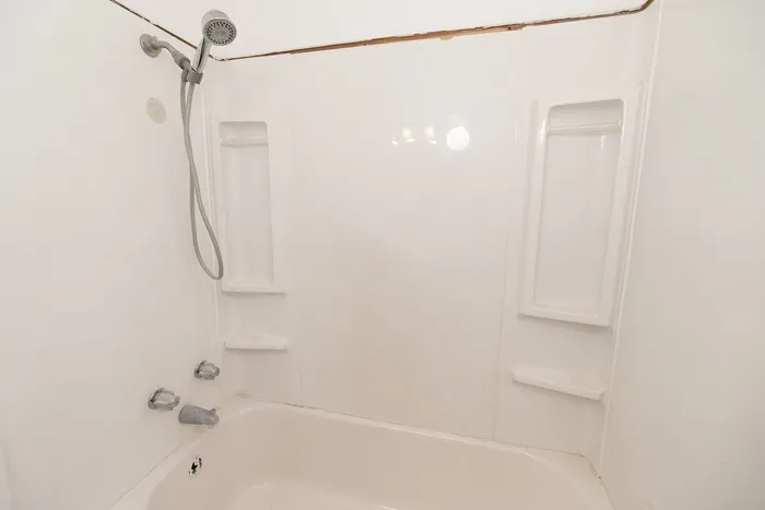 Bright bathroom featuring a pristine bathtub with modern chrome fixtures and convenient built-in shelving.