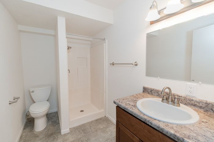 Modern bathroom featuring sleek white fixtures, granite countertop, and a spacious walk-in shower.