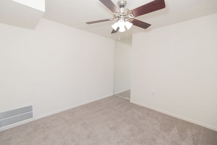 Inviting bedroom with plush carpet, mirrored closet, and modern ceiling fan in a bright, open space.
