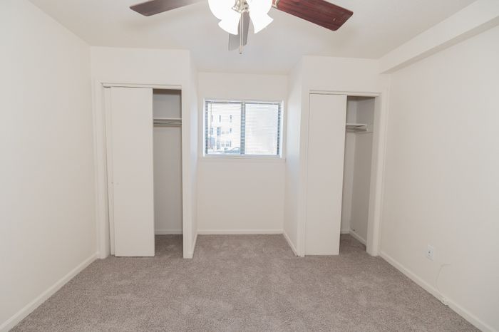Bright and cozy bedroom with plush carpet, dual closets, and a ceiling fan, perfect for modern living.