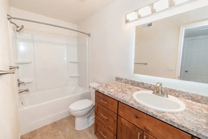 Renovated Chesterfield Village bathroom with a wood vanity, stone look countertop, large mirror, and white tub and shower.