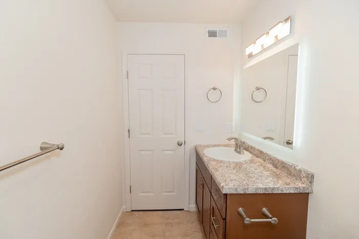 Renovated Chesterfield Village bathroom featuring a wood vanity, stone look countertop, large mirror, and towel bars.