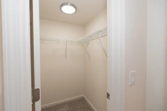 Walk in closet in a renovated Chesterfield Village apartment with white wire shelving, carpet, and overhead lighting.