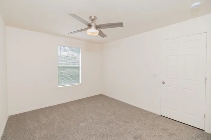 Spacious renovated bedroom at Chesterfield Village with gray carpet, a ceiling fan, window, and double closet doors.