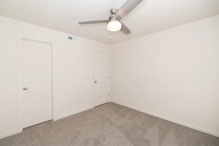 Bright renovated bedroom at Chesterfield Village with gray carpet, a ceiling fan, and two white interior doors.