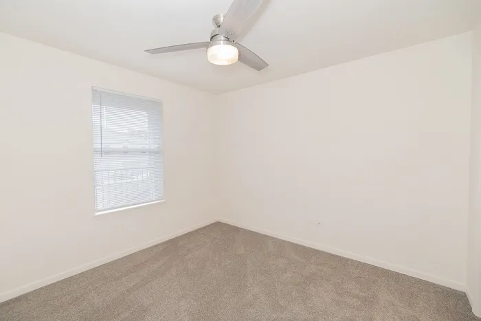 Renovated bedroom at Chesterfield Village with gray carpet, a ceiling fan, neutral walls, and a window with blinds.