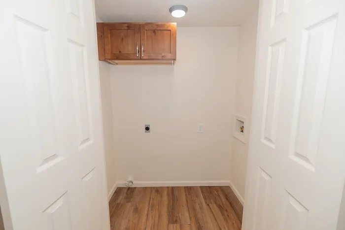 Laundry area in a renovated Chesterfield Village apartment with wood look flooring, overhead storage cabinets, and washer connections.