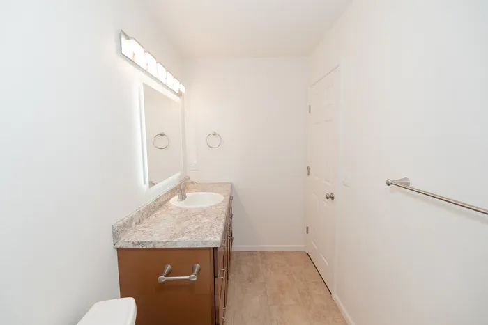 Renovated Chesterfield Village bathroom featuring a wood vanity, stone look countertop, large mirror, and towel bar.
