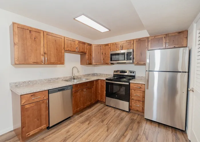 Renovated Chesterfield Village kitchen featuring wood cabinetry, stone look countertops, stainless steel appliances, and wood look flooring.