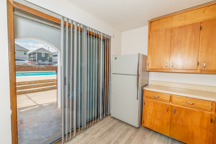 Bright kitchen with wooden cabinets, modern refrigerator, and sliding doors opening to a refreshing pool area.