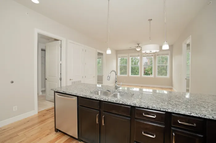 Sleek open-concept kitchen with elegant granite countertops and modern pendant lighting, showcasing a bright and airy living space with large windows.