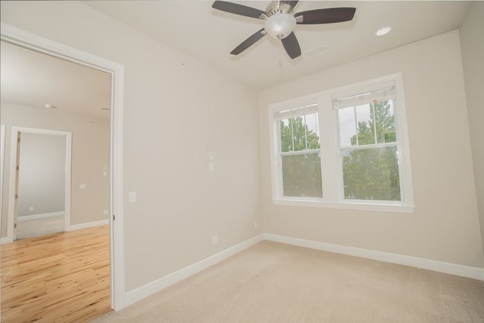 Bright and airy room with large windows and ceiling fan, featuring a seamless transition between soft carpet and elegant wood flooring.