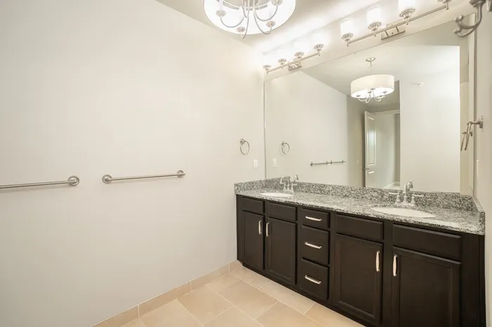 Elegant and modern bathroom featuring a sleek double sink vanity, stylish granite countertop, and spacious mirror with bright, chic lighting.