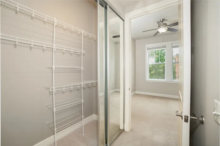 Bright and spacious walk-in closet with built-in shelving next to a serene, light-filled bedroom.