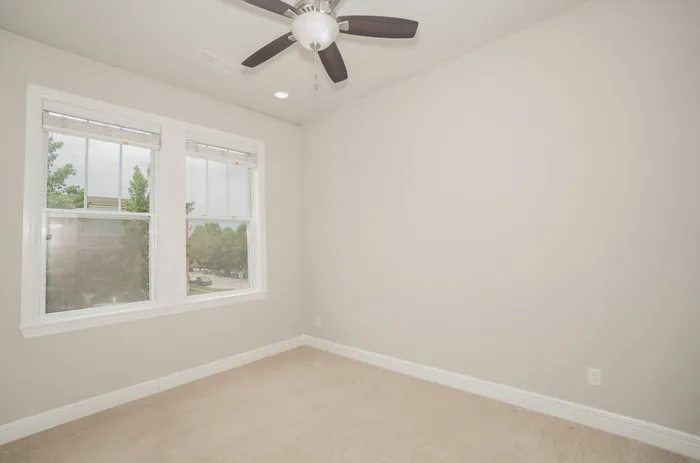 Bright bedroom with neutral tones, plush carpeting, and large windows inviting natural light.