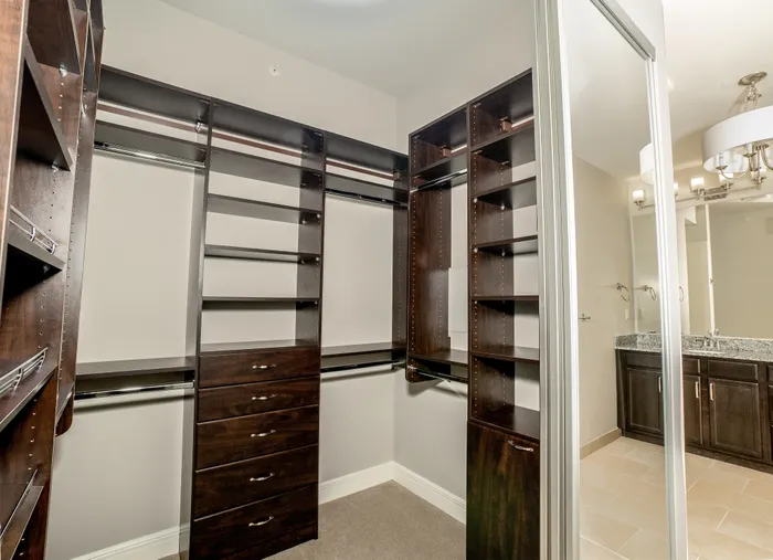 Elegant walk-in closet with rich wood shelving and modern fixtures adjacent to a sleek bathroom vanity.