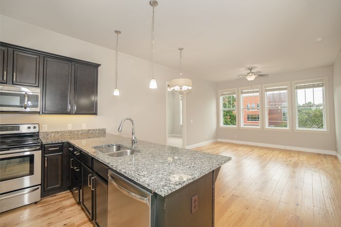 Modern open-concept kitchen with sleek granite countertops, stainless steel appliances, and bright living area with large windows overlooking greenery.