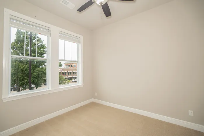 Bright and inviting room with large windows and a ceiling fan, offering a cozy ambiance and a view of lush greenery.