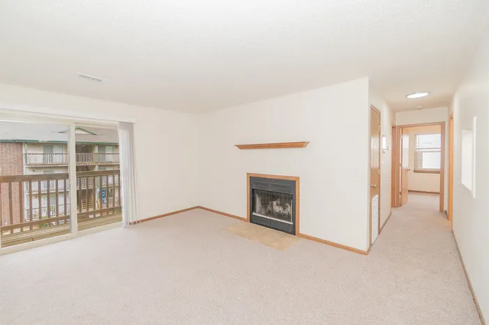 Polo Club Apartments living room with fireplace, sliding glass balcony door, neutral carpet, and hallway.
