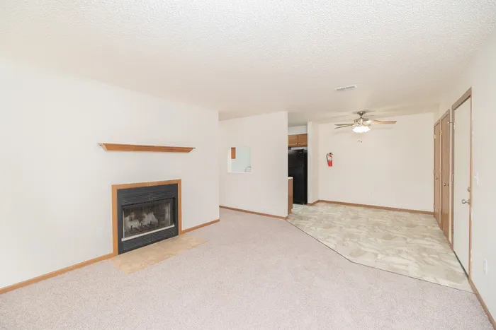 Open living and dining area at Polo Club Apartments featuring a fireplace, carpeted living room, and tiled dining space.
