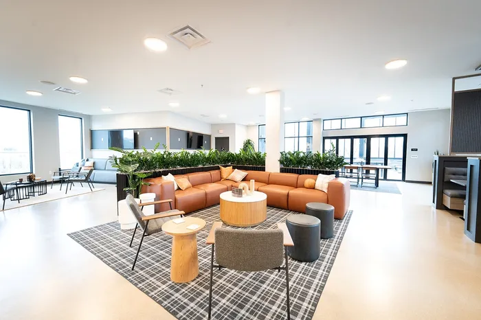 Spacious open-plan lounge featuring a modern tan sectional sofa, stylish decor, and vibrant greenery.