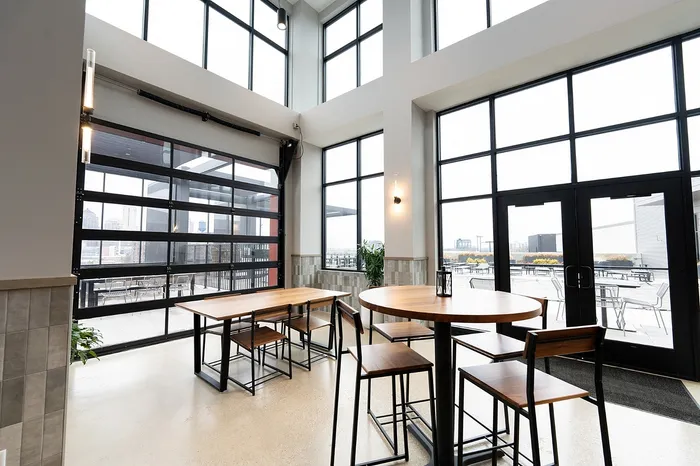 Modern dining space with high ceilings, large windows, and stylish wood furniture overlooking a terrace.
