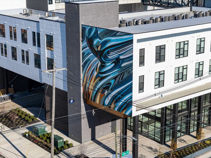 Modern apartment building with artistic mural, large windows, and urban landscaping.