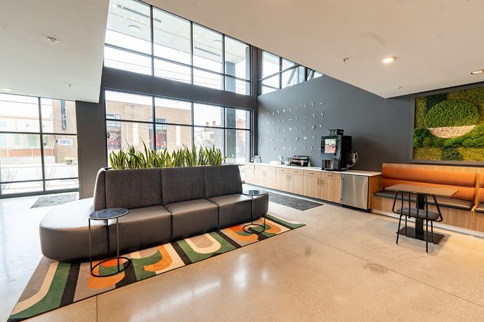 Modern apartment lobby featuring stylish seating, vibrant green wall art, and a refreshment bar with floor-to-ceiling windows.