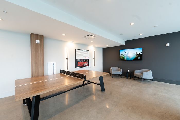 Stylish recreation room featuring a sleek wooden ping pong table, modern seating area, and vibrant wall art.