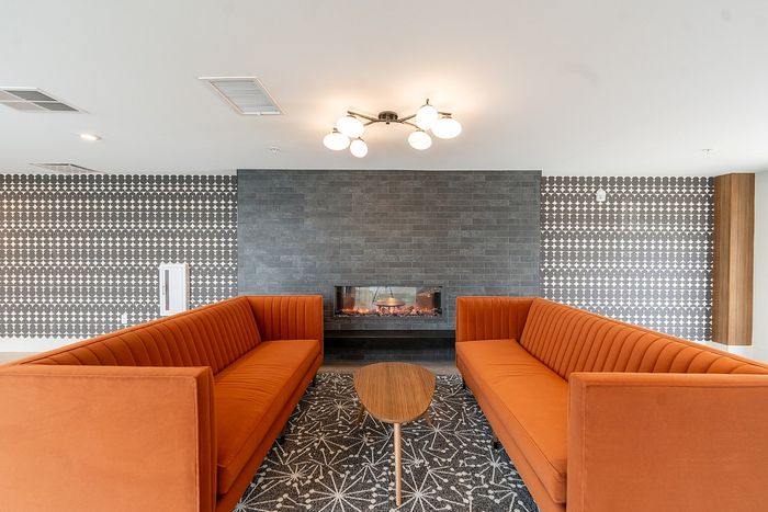 Contemporary living area featuring orange sofas, a sleek modern fireplace, and stylish patterned wallpaper, creating a warm and inviting atmosphere.