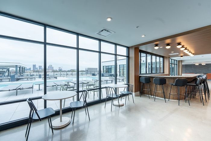 Modern urban lounge with floor-to-ceiling windows overlooking a chic rooftop pool and city skyline, featuring stylish bar seating and elegant dining tables.